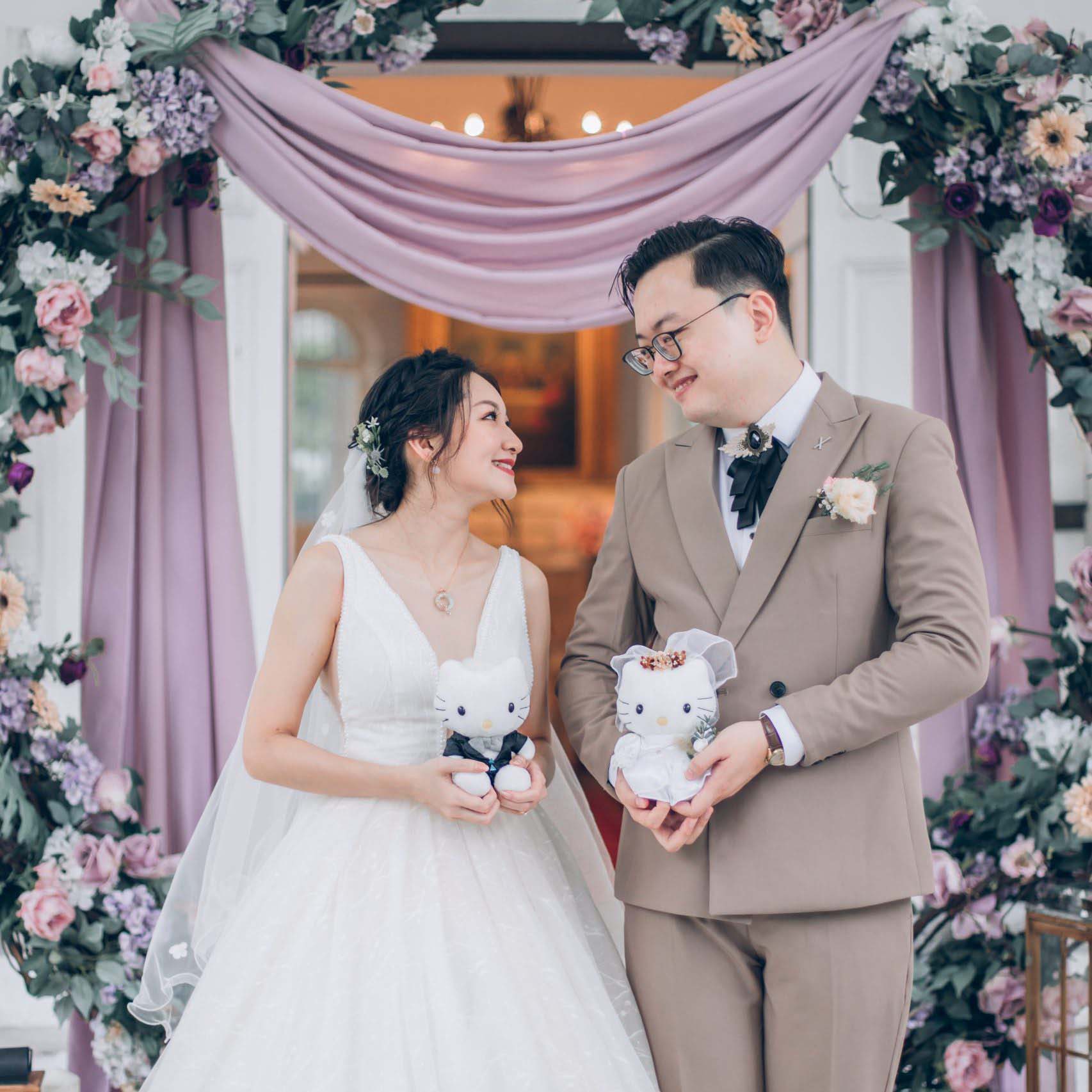 Groom and bride, looking at each other, hold a Hello Kitty plush toy